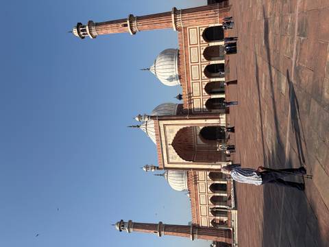       Wide courtyard of Jama Masjid with worshippers and a man with a cane in the foreground.
  