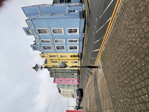       Row of pastel-colored Georgian terraced houses on a quiet street under grey skies.
  