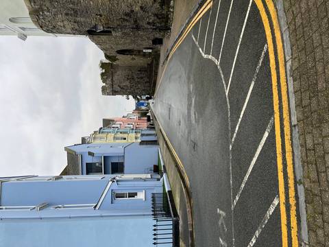       Empty wet street lined with pastel houses and an ancient stone gate on a rainy day.
  