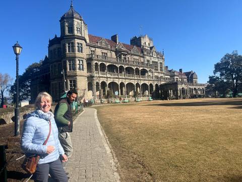       Smiling travellers stand on a cobblestone path in front of the historic Viceregal Lodge with clear blue skies overhead.
  