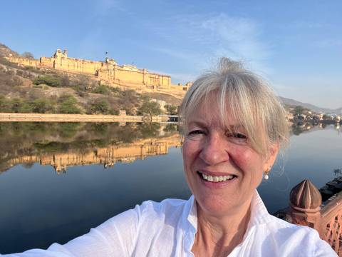       Selfie of traveller with the golden-hued Amber Fort reflecting in the calm lake behind her.
  