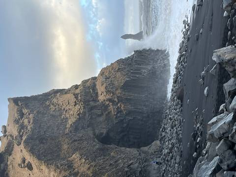       Basalt cliffs at Reynisfjara black beach with ocean spray crashing high against the rocks.
  