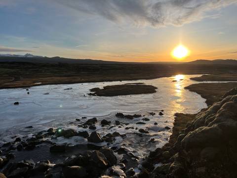       Sun setting over an icy Icelandic river with shimmering reflections across frozen surfaces.
  