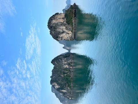       Emerald waters reflecting tall limestone islands under a blue sky with wispy clouds.
  