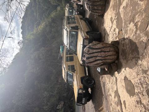       Two beige safari jeeps parked beside a striped boulder at a dusty base camp.
  