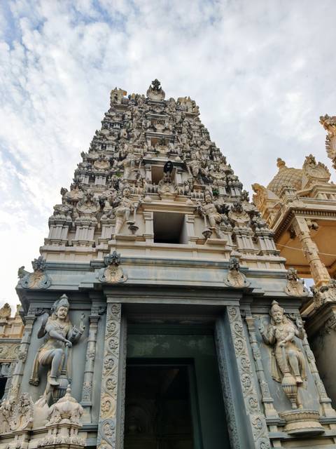       Ornate gopuram of a Hindu temple richly decorated with sculptures against the sky.
  