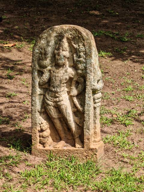       Close-up of an ancient stone guardian carving standing on earthen ground with sparse grass.
  