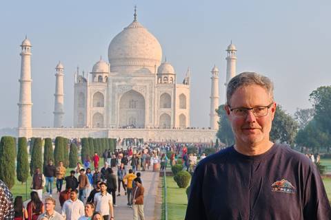       Male traveler poses in front of the Taj Mahal with crowds lining the gardens.
  