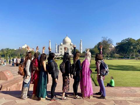       Group of travelers raise hands toward the Taj Mahal on a sunny morning.
  