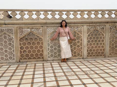       Woman poses against an ornate lattice stone wall with geometric carvings.
  