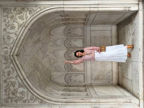       Woman raises hand inside a marble alcove decorated with floral carvings.
  