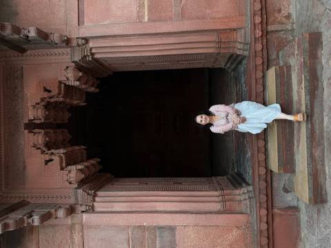       Woman sits on sandstone steps within a dark arched entrance at Fatehpur Sikri.
  