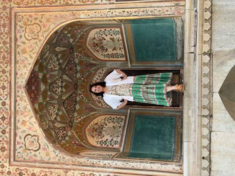       Woman poses confidently in a colorful Mughal archway with floral artwork.
  