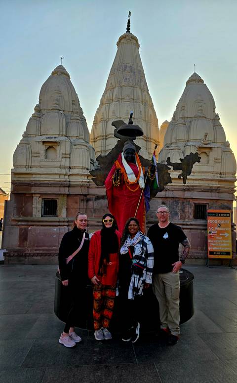       Small tour group posing in front of a garlanded statue and temple spires at dusk
  