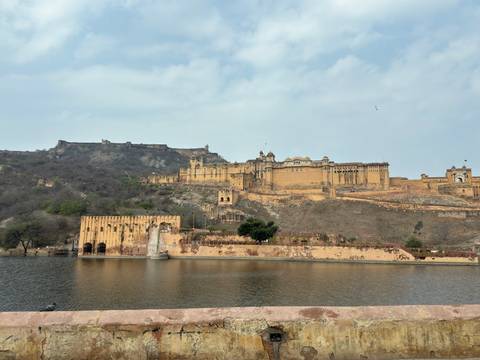       Panoramic view of Amber Fort sprawling across a rocky hillside with reflection in Maota Lake
  