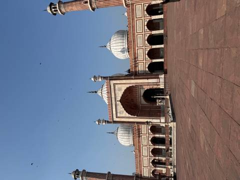       Wide view of a grand red-sandstone mosque with white domes under a clear blue sky
  