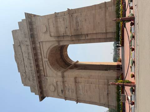       Stone triumphal arch of India Gate towering against a pale sky
  