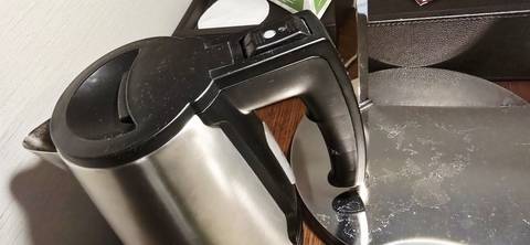       Stainless steel electric kettle placed on a smudged metal lamp base in a hotel room.
  
