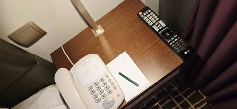       Hotel bedside table with telephone, pencil, notepad and TV remote neatly arranged.
  