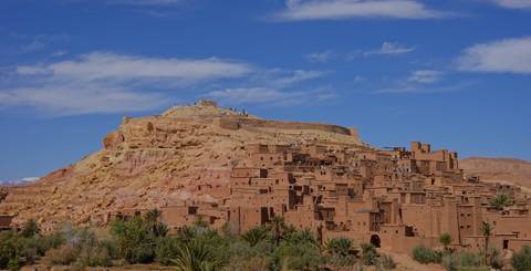       Clay-colored buildings of Ait Benhaddou climb a rocky hilltop beneath a bright blue Moroccan sky.
  
