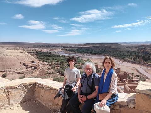       Three travellers pose at a panoramic lookout over the Ounila valley and fortified ksar of Ait Benhaddou.
  