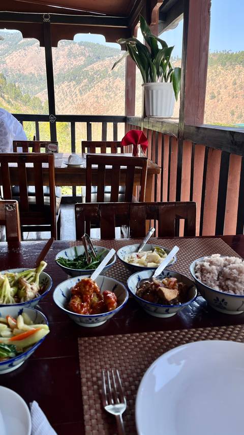       Tabletop spread of traditional Bhutanese dishes in a rustic wooden restaurant interior.
  