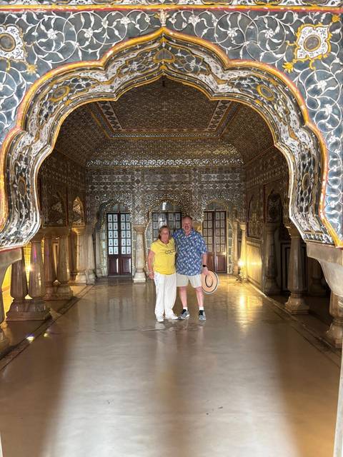       Couple standing inside the glittering Sheesh Mahal mirror hall at Amer Fort.
  
