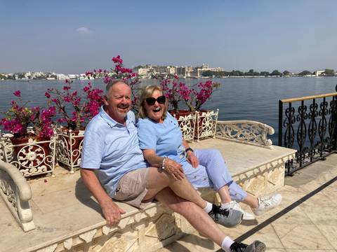       Laughing couple seated on a marble bench overlooking Lake Pichola and Udaipur’s city palace.
  