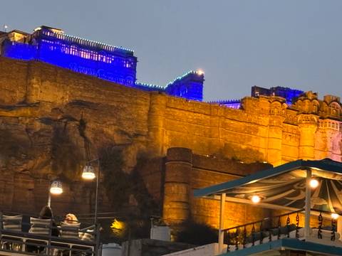       Night view of the illuminated Mehrangarh Fort walls glowing blue and gold above Jodhpur.
  