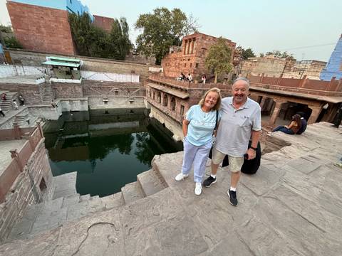       Couple standing by the historic stepwell Toorji Ka Jhalra in Jodhpur with green water below.
  