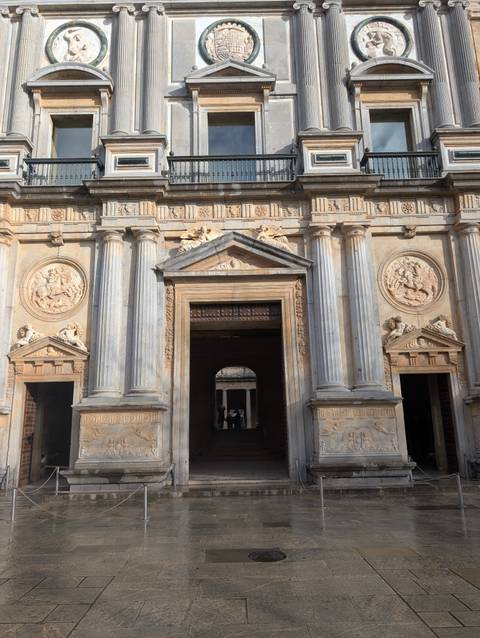       Classical stone entrance with Corinthian columns and sculpted medallions lit by warm sun.
  
