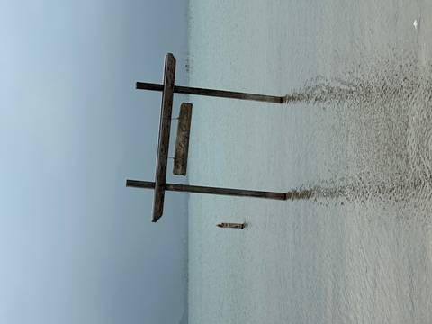       Lonely wooden swing frame standing in calm, misty coastal waters on an overcast day.
  