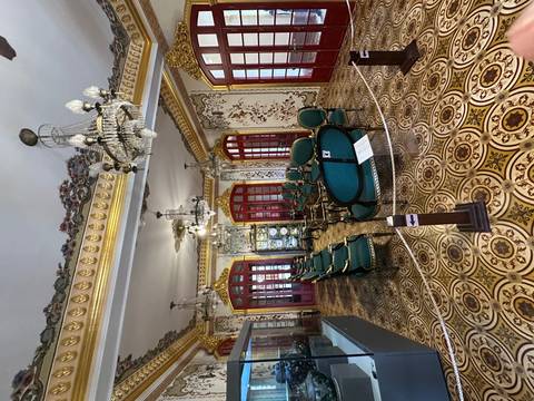       Lavish colonial-era salon with patterned tiled floors, green velvet chairs, gilded mouldings and glittering chandeliers.
  