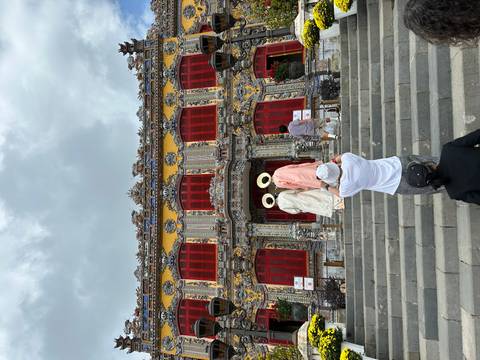       Visitors ascend stone steps toward a richly decorated imperial-style palace façade adorned with mosaics and red windows.
  