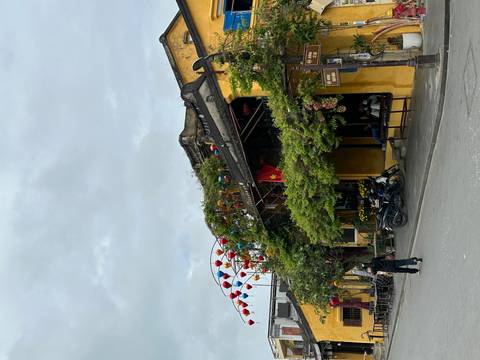       Charming yellow merchant house in Hoi An adorned with lanterns; a lone person walks by on the street.
  