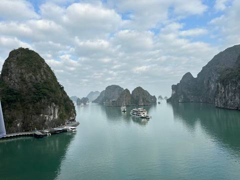       Serene vista of jade waters and towering limestone pinnacles of Ha Long Bay with cruise ships sailing.
  