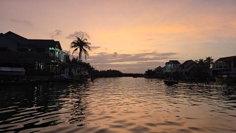       Calm river lined with houses and a lone palm tree reflects soft pastel colors at dusk.
  