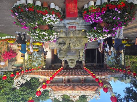       Visitors explore a festive temple courtyard decorated with lanterns, flowers and a laughing Buddha statue.
  