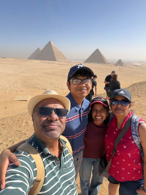       Family selfie with the pyramids of Giza in the background on a bright desert day.
  
