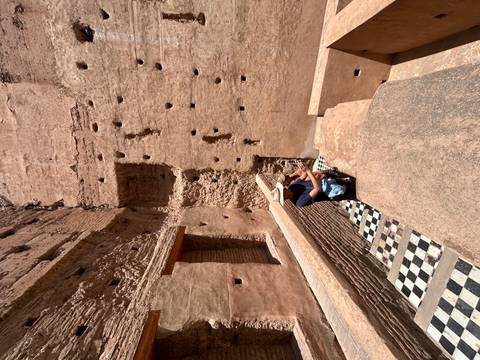       Solo traveller sitting on black-and-white tiled steps inside ancient adobe walls with sun overhead
  
