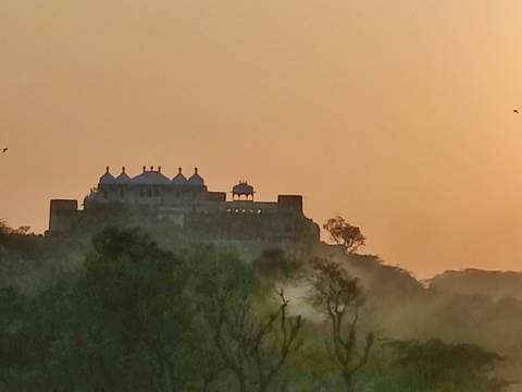       Distant hilltop palace silhouetted against an orange sunset haze
  