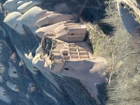       Eroded stone church carved into fairy-chimney formations on a barren hillside.
  
