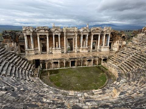       Panoramic view of a well-preserved Roman amphitheatre surrounded by hills.
  