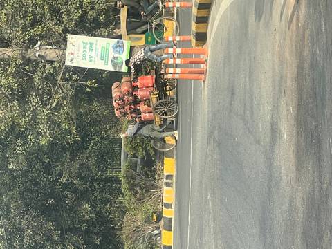       Roadside scene with a man pedalling a cart stacked high with LPG cylinders in busy Delhi traffic.
  