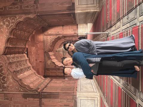       Family group smiles for the camera inside the richly patterned interior of a historic mosque.
  