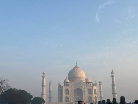       Distant view of the Taj Mahal domes under a hazy blue morning sky with empty space above.
  