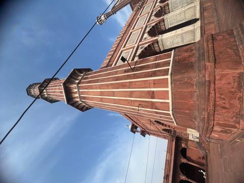       Tall striped sandstone minaret of Jama Masjid shot from ground level with overhead wires cutting across.
  