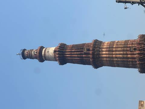       Tall red-sandstone Qutub Minar tower rising against a clear blue Delhi sky with a small airplane in the distance.
  