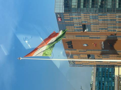       Large Indian tricolour flag waving on a tall pole beside modern glass offices bearing corporate logos.
  