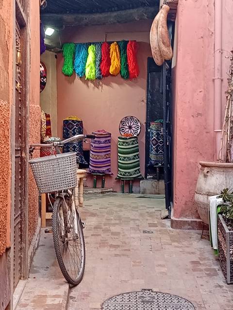       Colorful woven baskets stacked outside a pink-walled alley with a bicycle in Marrakesh medina.
  